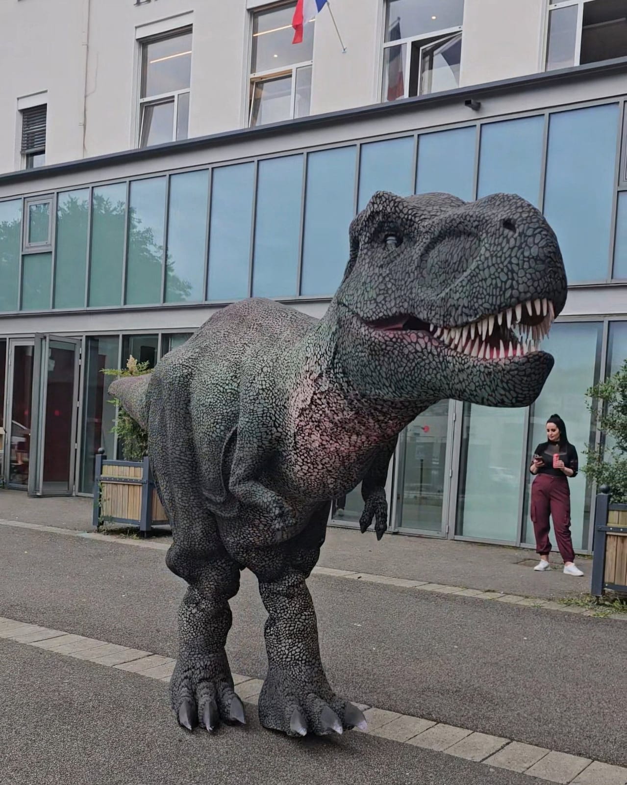Le Giga Rex de Mascotte Dreams, gueule ouverte, devant un bâtiment