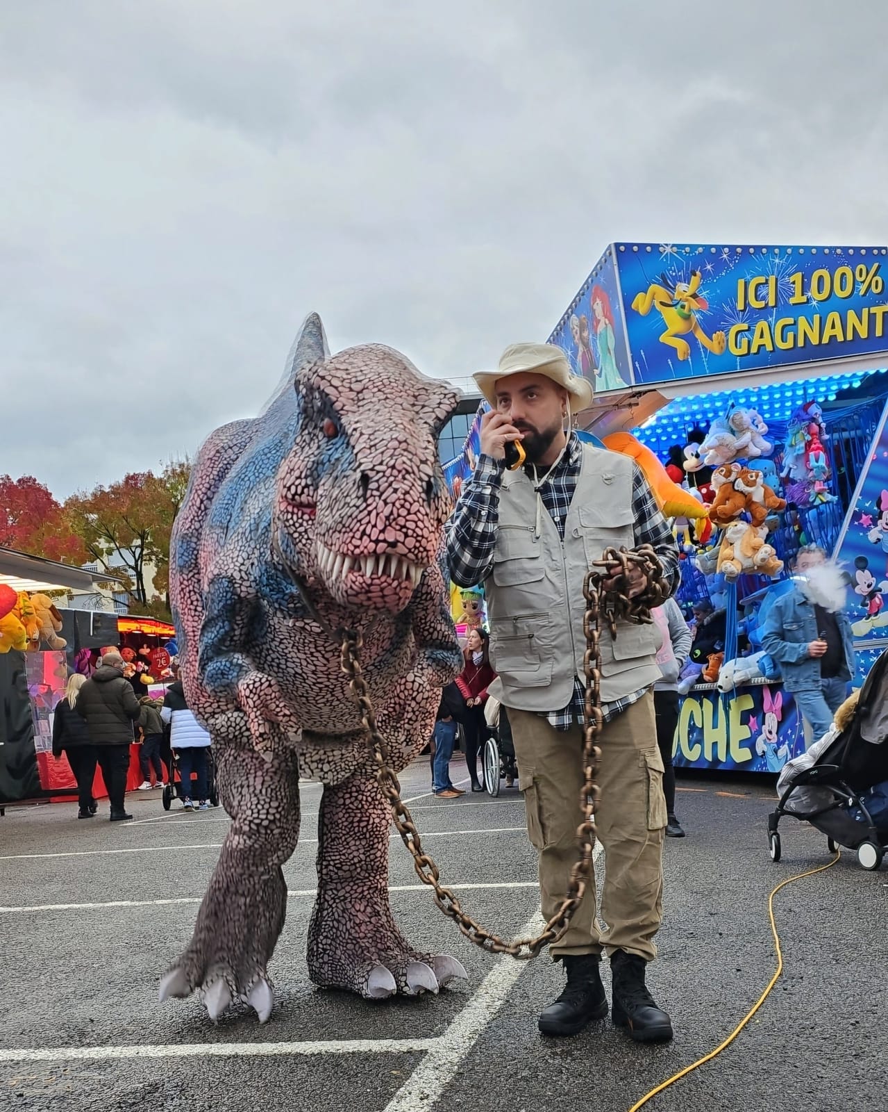 Le T-Rex animé de Mascotte Dreams, tenu en laisse par son soigneur dans une fête foraine